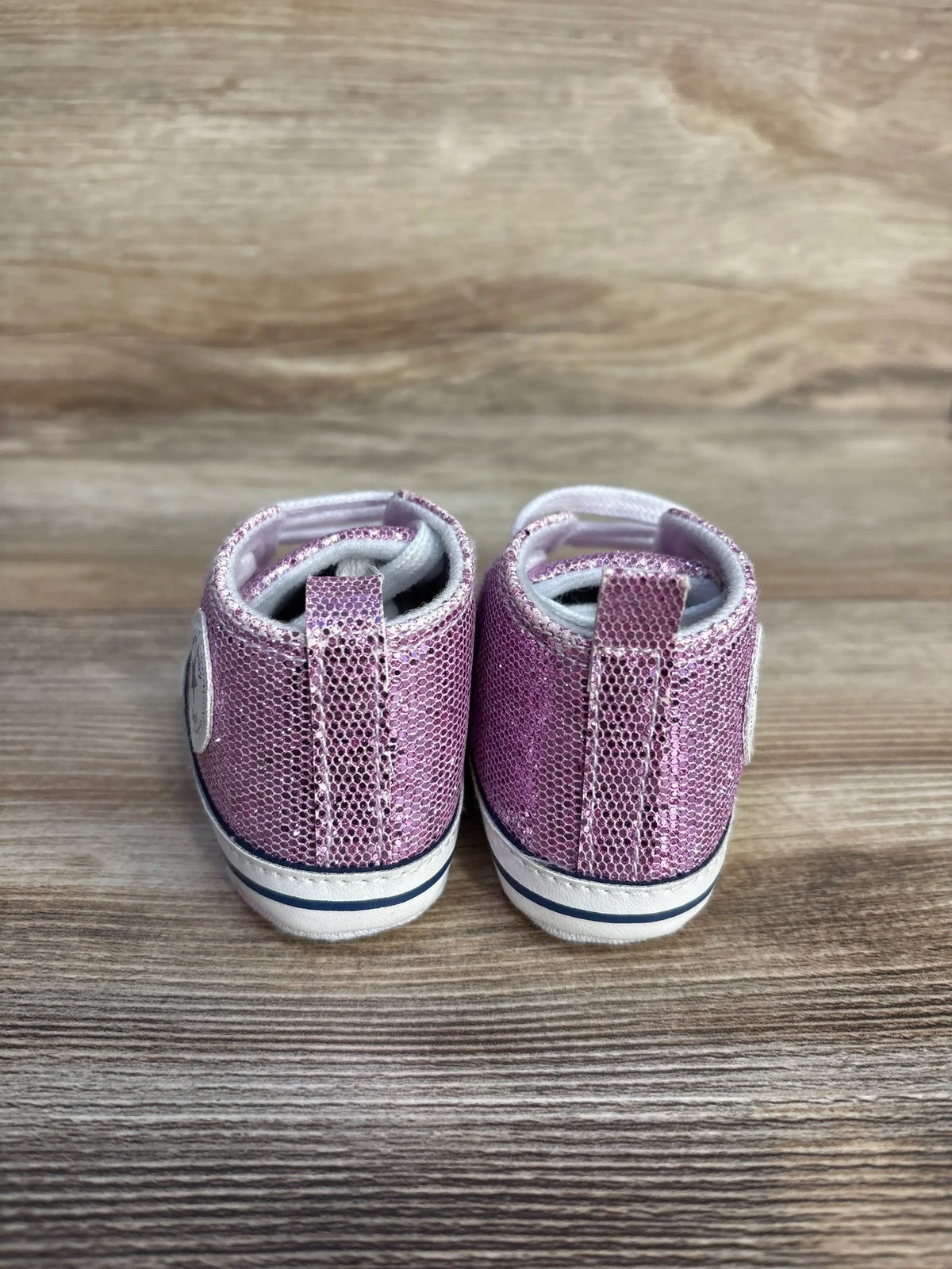 Rear view of purple glittery slip-on crib shoes by Me n Mommy To Be on a wooden surface.