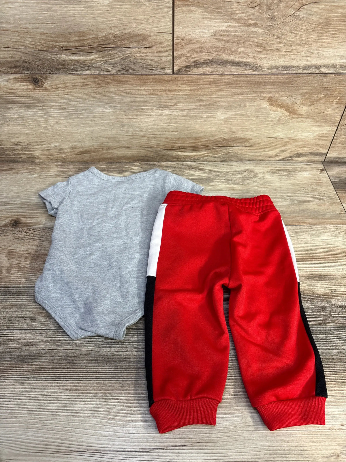 Top-down view of Reebok 2-piece baby set, grey short-sleeve bodysuit and red joggers with white and black side panels on wood background
