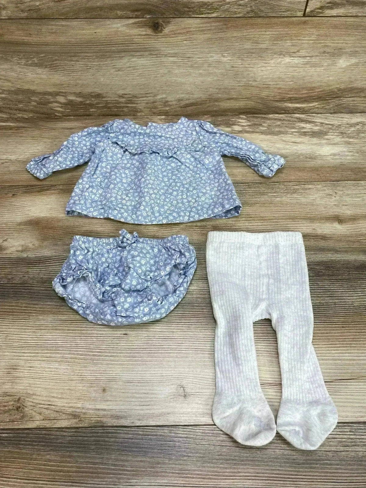 Flat lay of Just One You 3pc blue floral set showing ruffled top, matching bloomers and light ribbed tights on wood floor