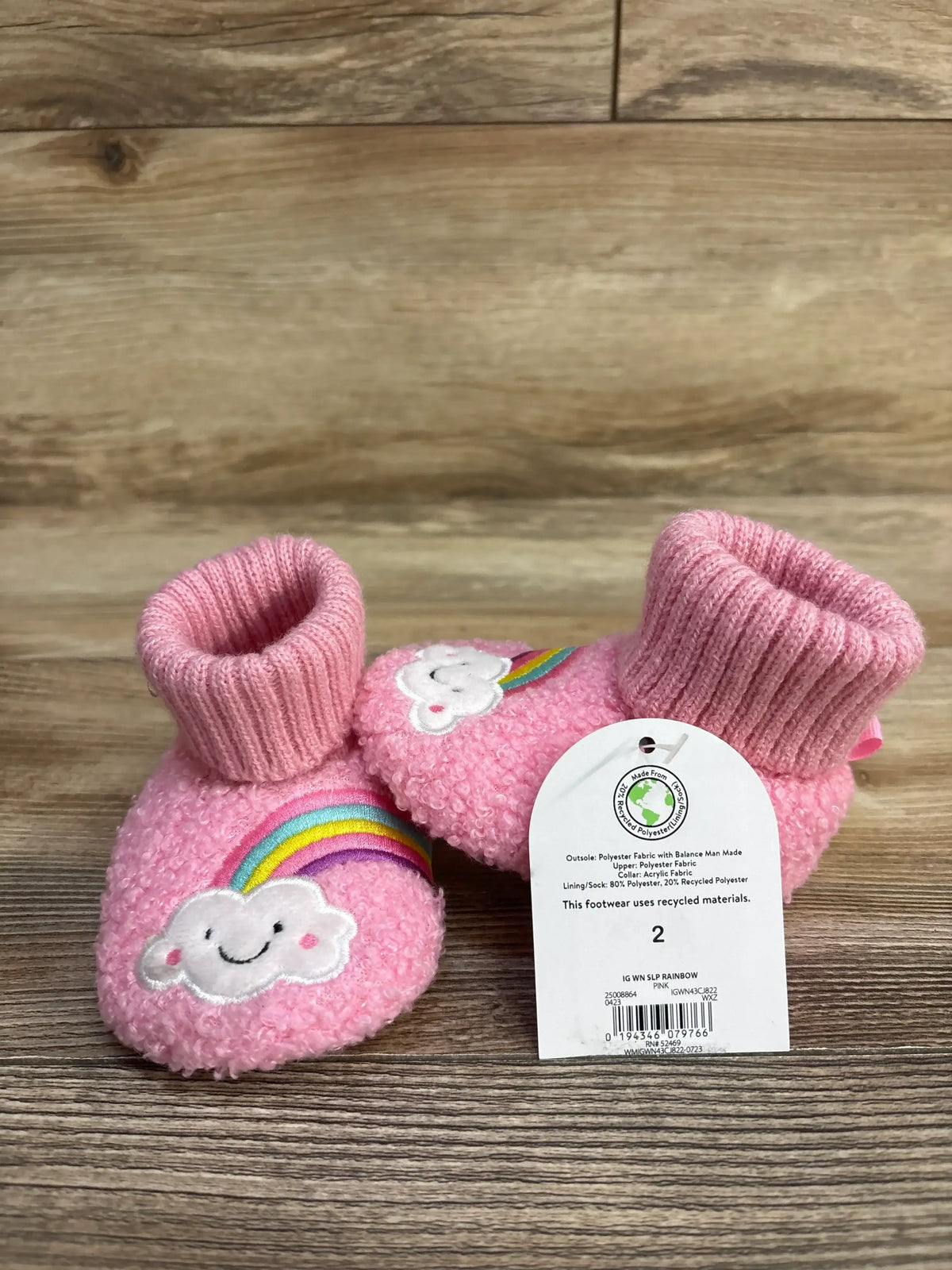 Pink baby booties with rainbow and cloud embroidery, eco-friendly, on wooden background