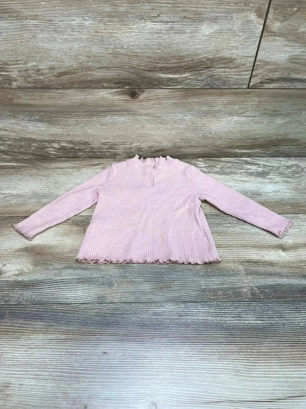 Flat lay of Old Navy pink ribbed long sleeve shirt size 6-12m showcasing lettuce trim hem and cuffs on wood plank floor