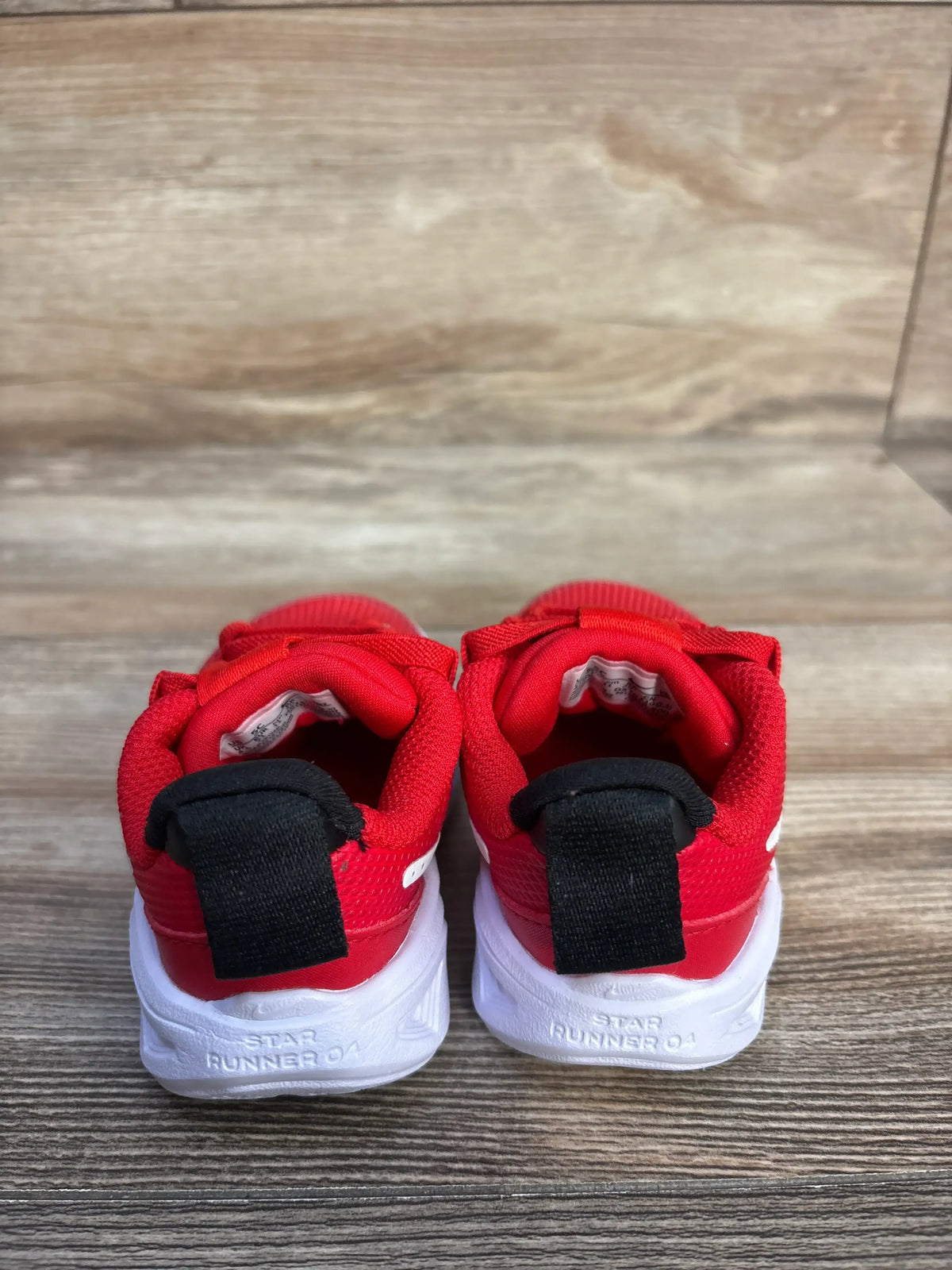 Rear view of Nike Star Runner 4 TD University Red sneakers showcasing black heel tabs and white soles on a wood floor