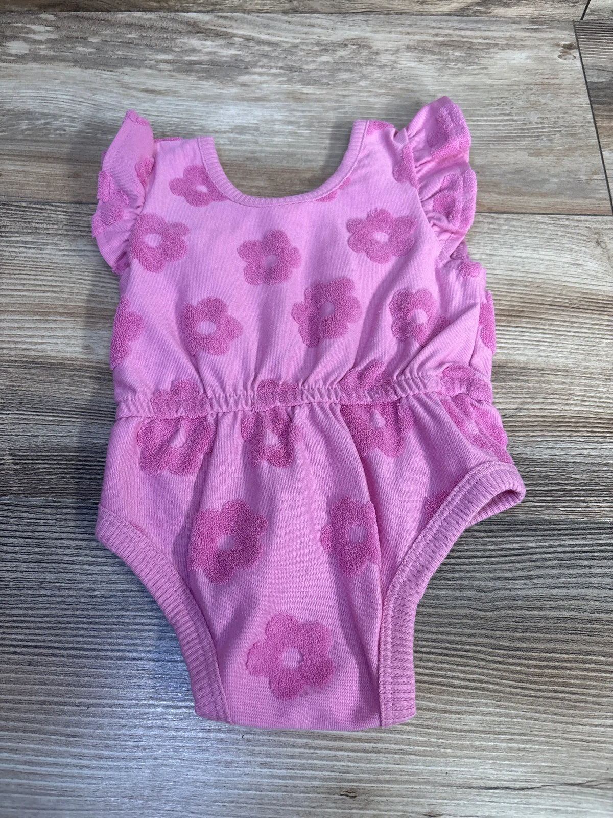 Front view of PL Baby pink tank bubble romper showcasing its flower pattern and bubble hem on a wood-grain surface