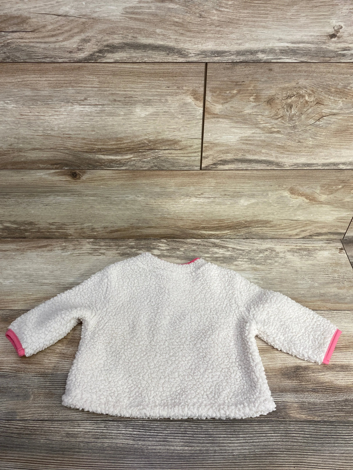 Gently used white sherpa baby jacket with pink trim on cuffs on wooden floor background