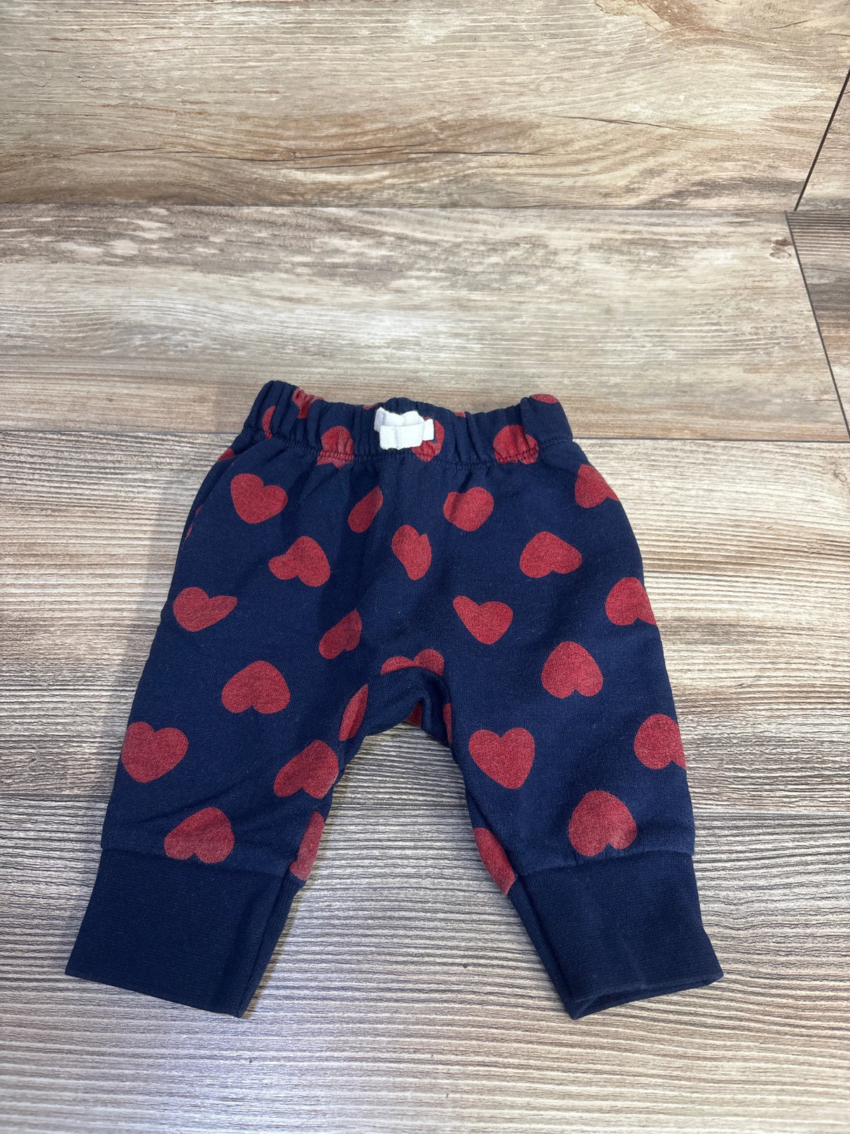 Flat lay of Cat & Jack baby joggers (0-3M) navy with red hearts, elastic waist and cuffed ankles on wood background