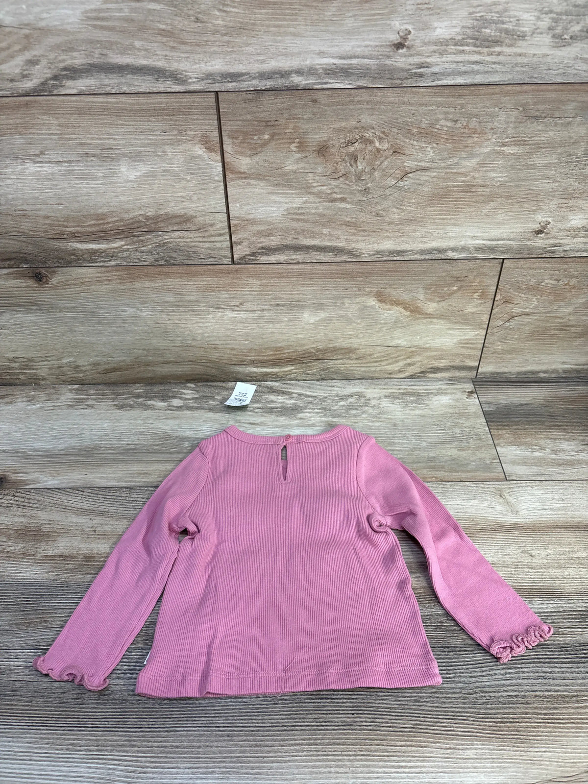 Front view of pink Baby Gap ribbed long sleeve shirt in size 12-18 months showcasing lettuce sleeve trim on wood background