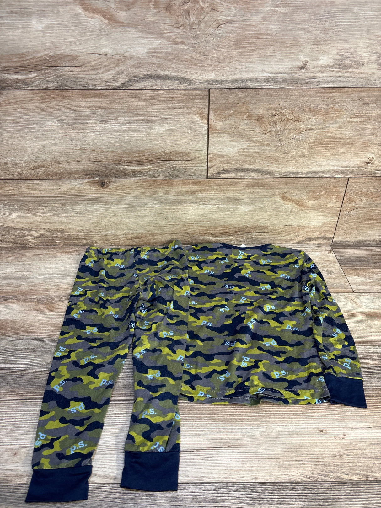 Kids camo pajama set with long sleeves and pants, green and black pattern on wood floor