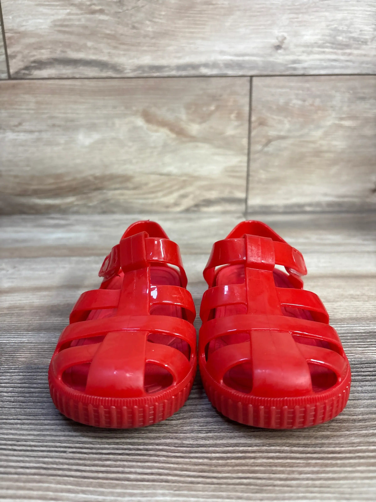 Front view of red jelly fisherman sandals in size 8 9C showcasing hook and loop closures on a wood look floor