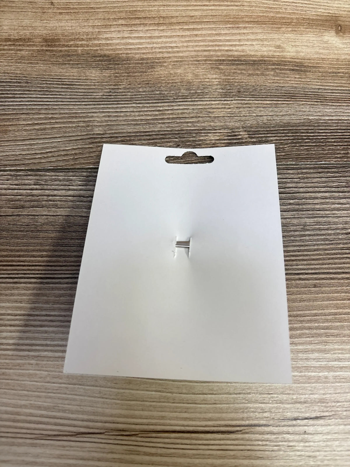 Blank white product tag with hanging hole on wood surface, ready for kids or maternity item labeling