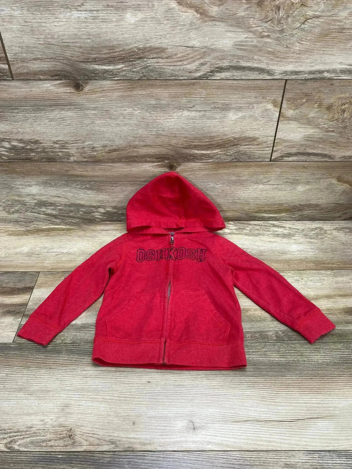 Flat lay of OshKosh red full-zip toddler hoodie (3T) showing front with hood and kangaroo pockets on wood floor