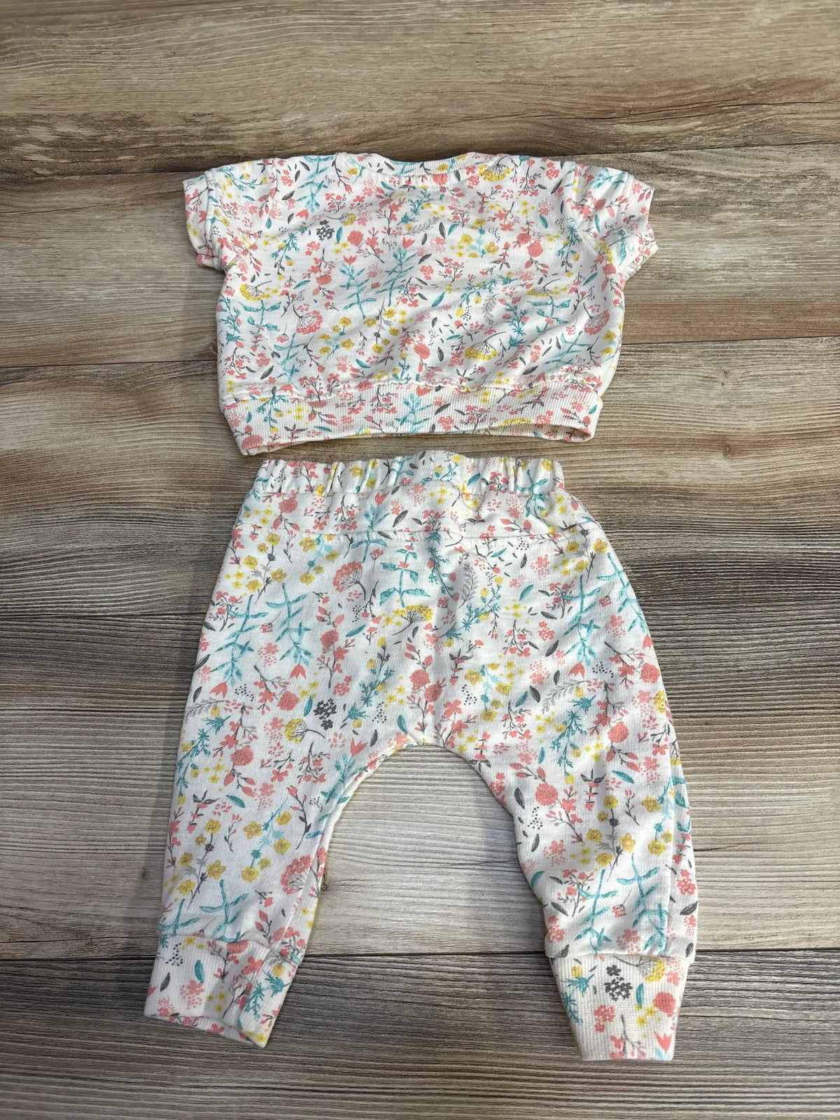 Flat lay of baby two-piece floral top and pants with elastic waistband, ribbed cuffs, multicolor flowers on wood background