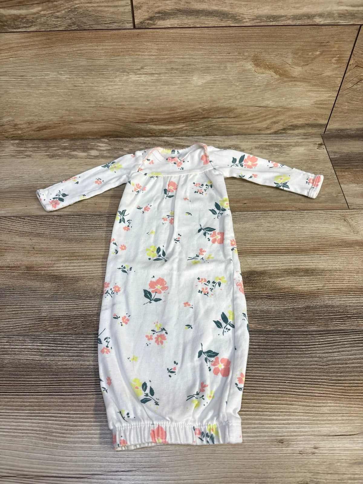 Top-down view of Carter’s preemie sleep gown showcasing pink and yellow floral print, long sleeves, and elastic gathered bottom on a wood floor