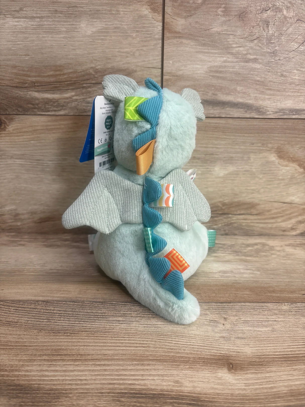 Plush dragon toy with textured wings, colorful ribbons, and soft fabric on wooden background