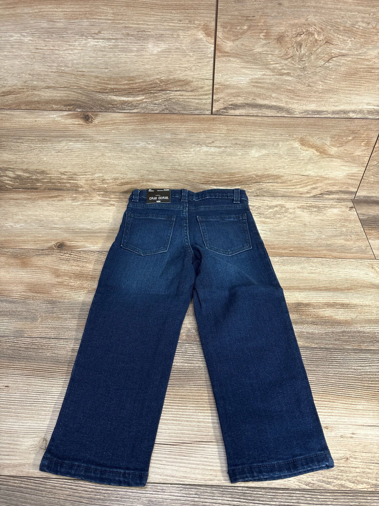 Back view of dark blue toddler jeans with pockets on wooden floor
