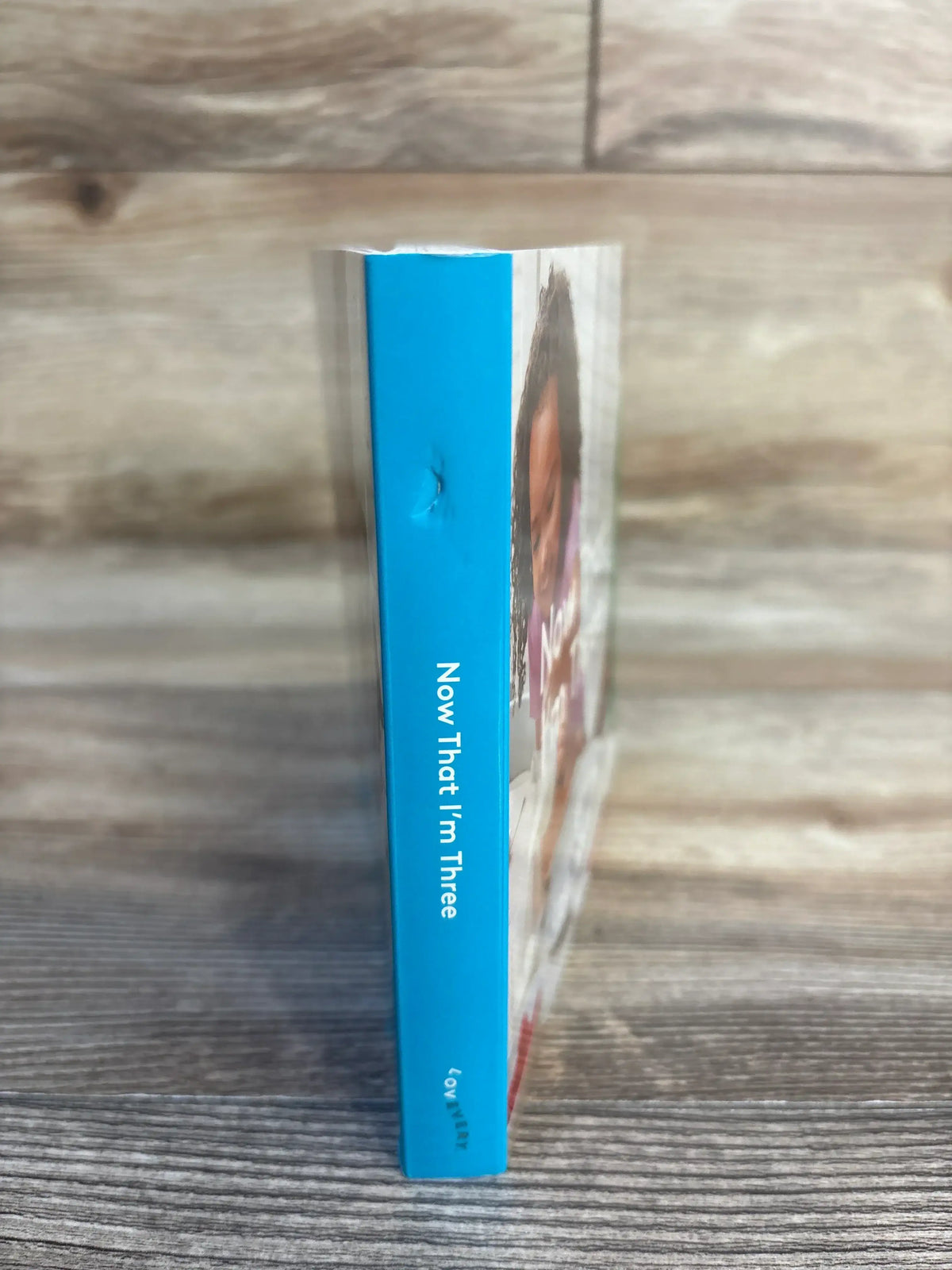 Children’s book with blue spine titled 'Now That I’m Three' on wood background