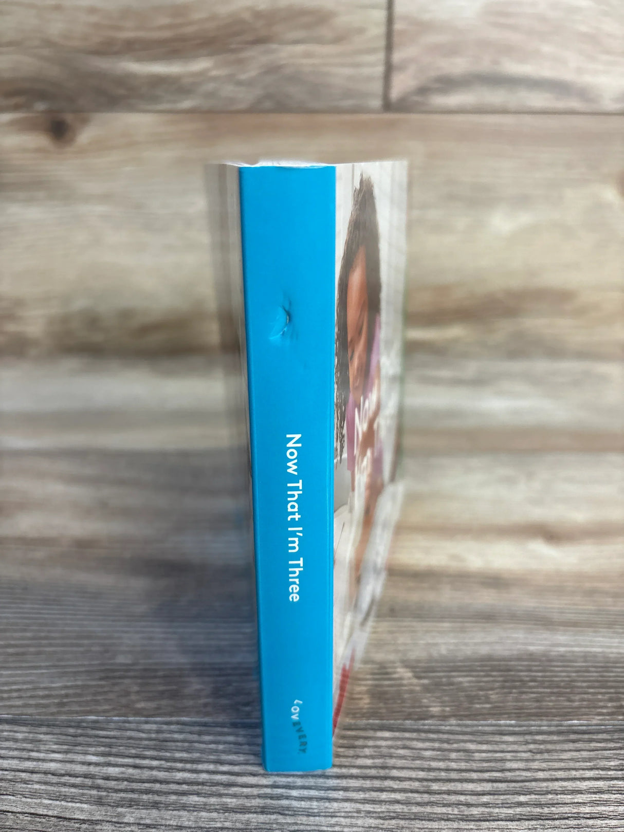 Children’s book with blue spine titled 'Now That I’m Three' on wood background