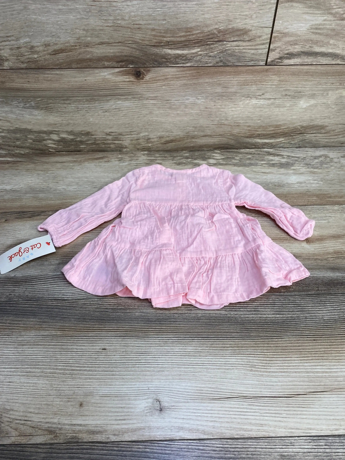 Back view of pink Cat and Jack muslin tiered baby dress with long sleeves and matching bloomers on light wood background