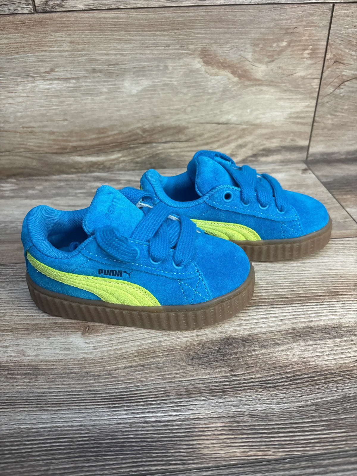 Blue suede toddler sneakers with yellow stripe and gum soles on wooden floor