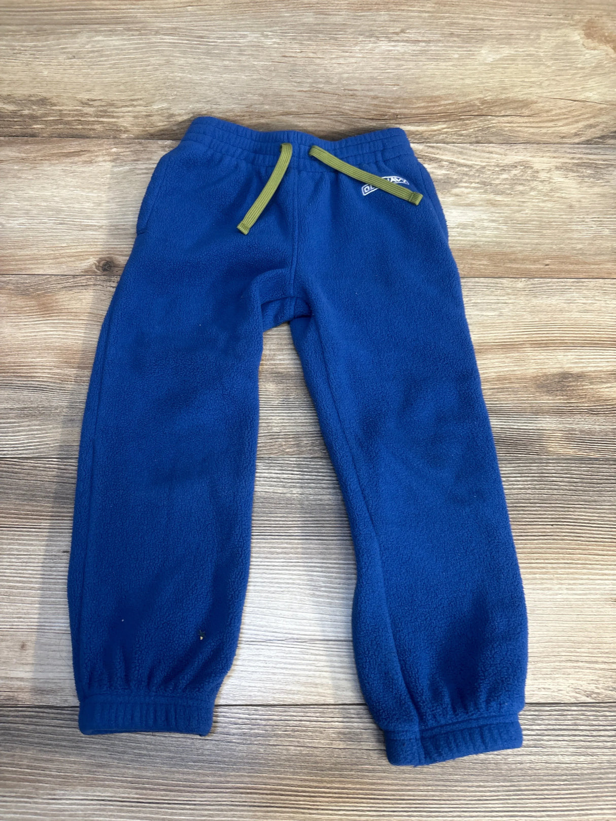 Blue fleece toddler pants with green drawstring on wood background