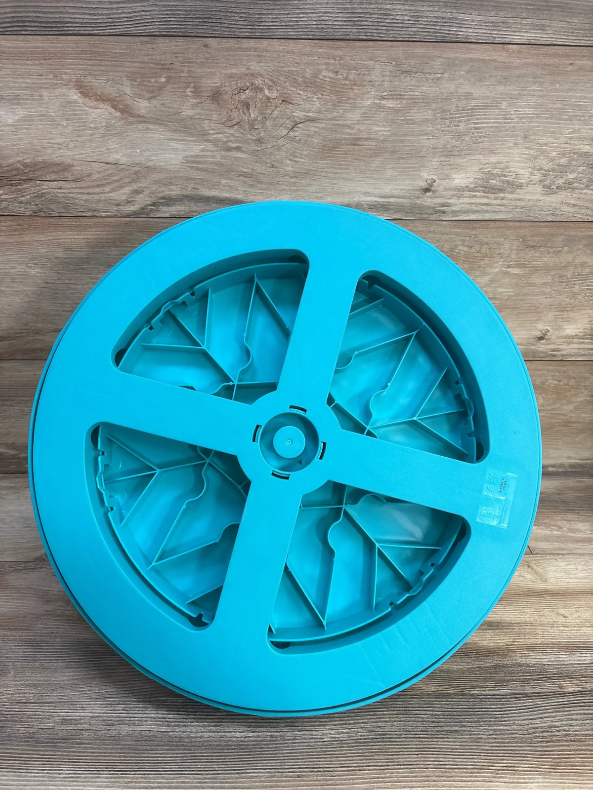 Bottom view of B. Toys Twirly Time spinning activity toy showing blue circular base with recessed underside on wood floor