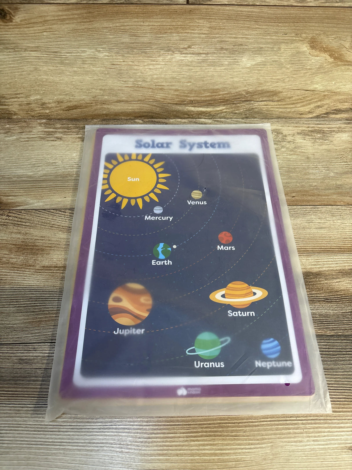 Colorful laminated solar system learning chart for kids on a wood surface