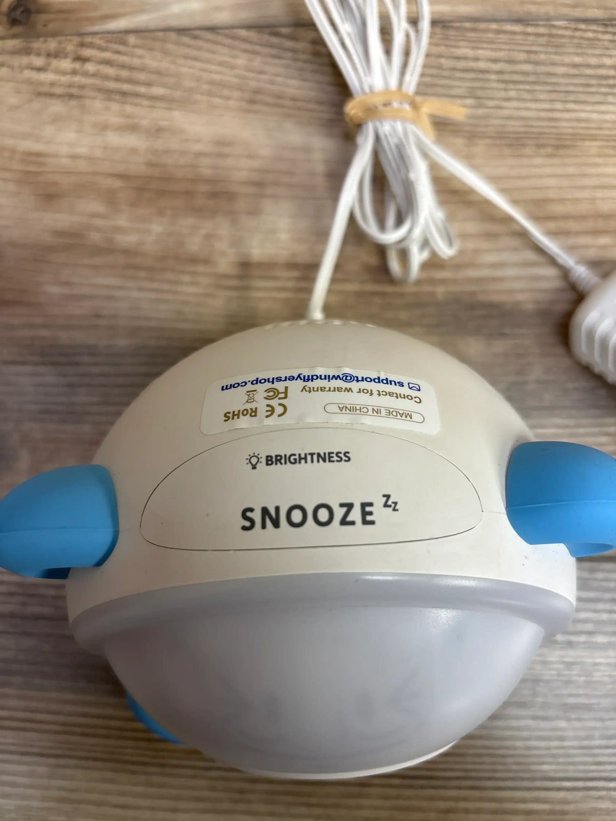 Close-up view of WindFlyer Sleep Training OK to Wake Clock with blue ears, snooze and brightness controls on a wood surface