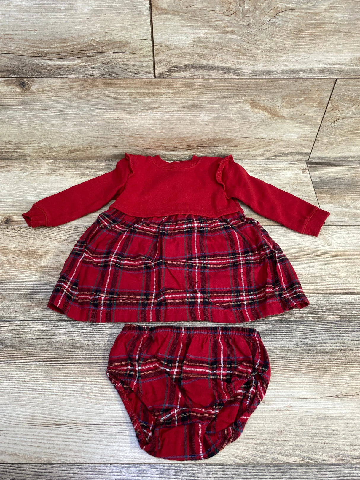 Red long-sleeve baby dress with ruffle shoulders and matching plaid diaper cover on wooden floor