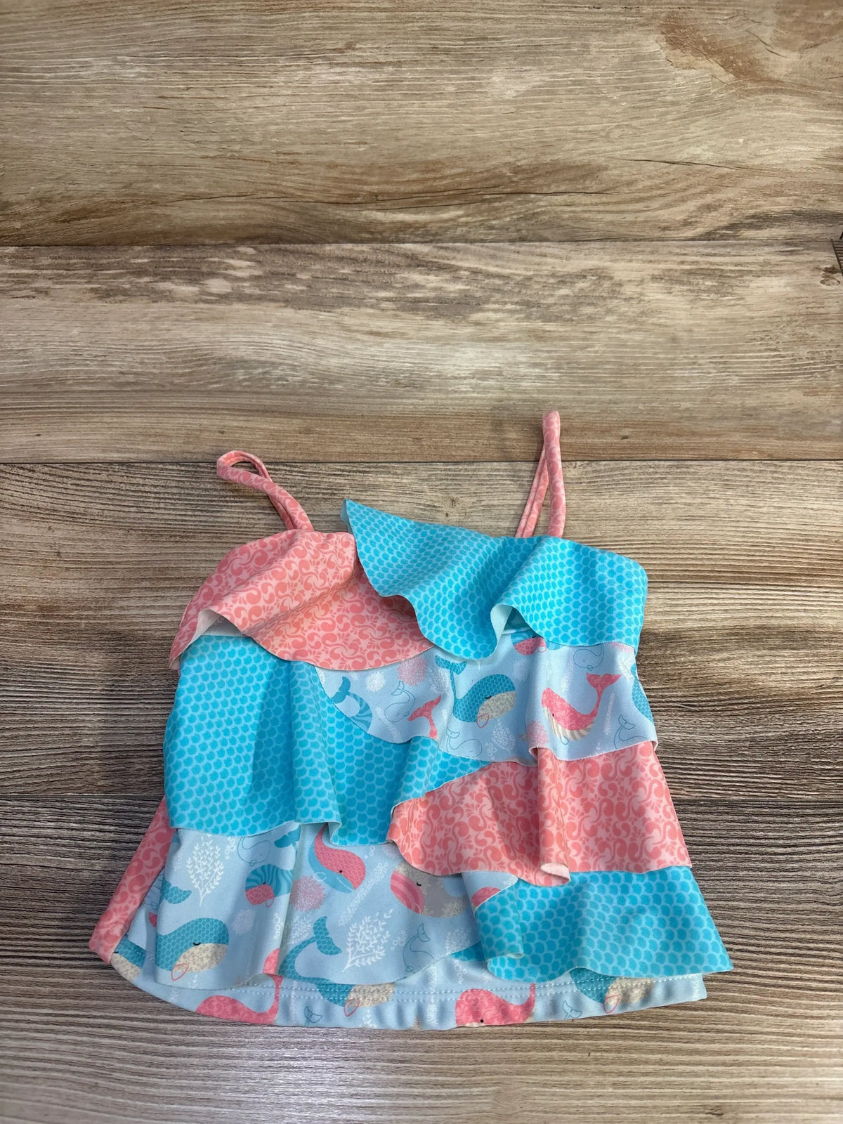 Flat lay of girls tank swim top, size 2T, showcasing layered ruffle tiers and blue and pink mermaid print with thin straps on wood background