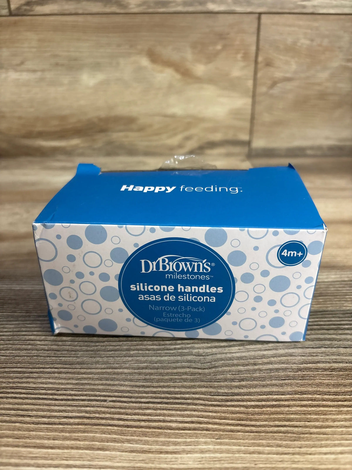 Front view of Dr Browns Milestones silicone narrow bottle handles three pack packaging showing Happy feeding text on a wood surface