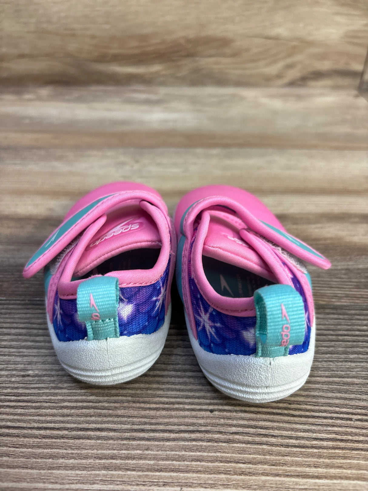Rear view of Speedo Shore Explorer toddler water shoes showcasing pink uppers, blue star-pattern heel panels, pull tabs and white non-slip soles on wood surface