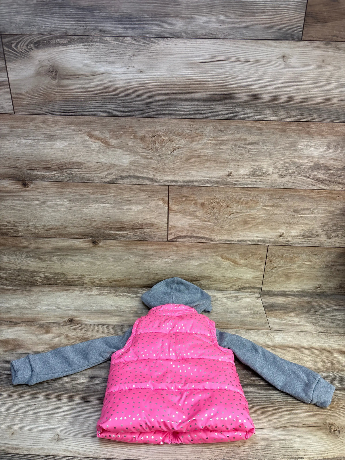 Back flat lay of pink 2fer puffer jacket showing grey hooded sleeves and silver dot print on wood plank background