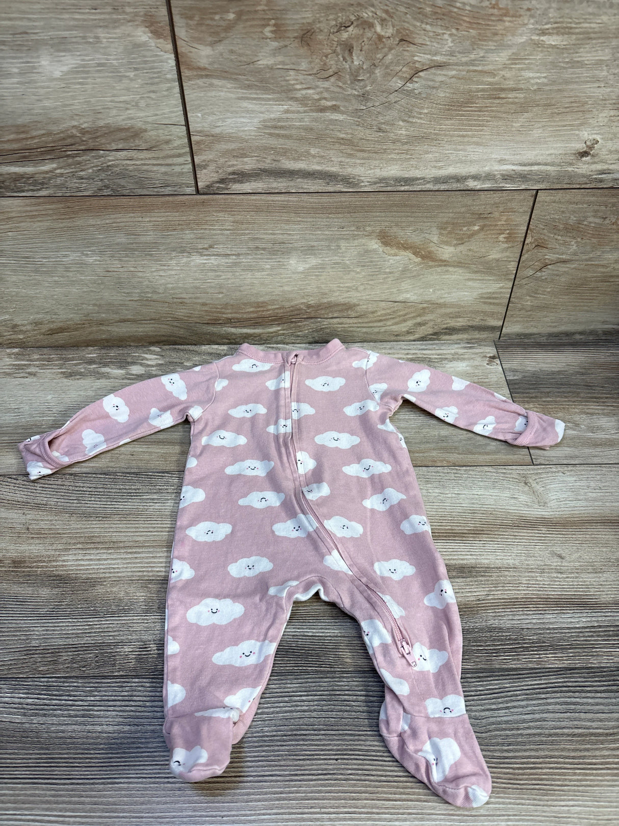 Top-down view of Old Navy pink cloud-print footed sleeper showcasing diagonal zipper and footed legs on light wood background