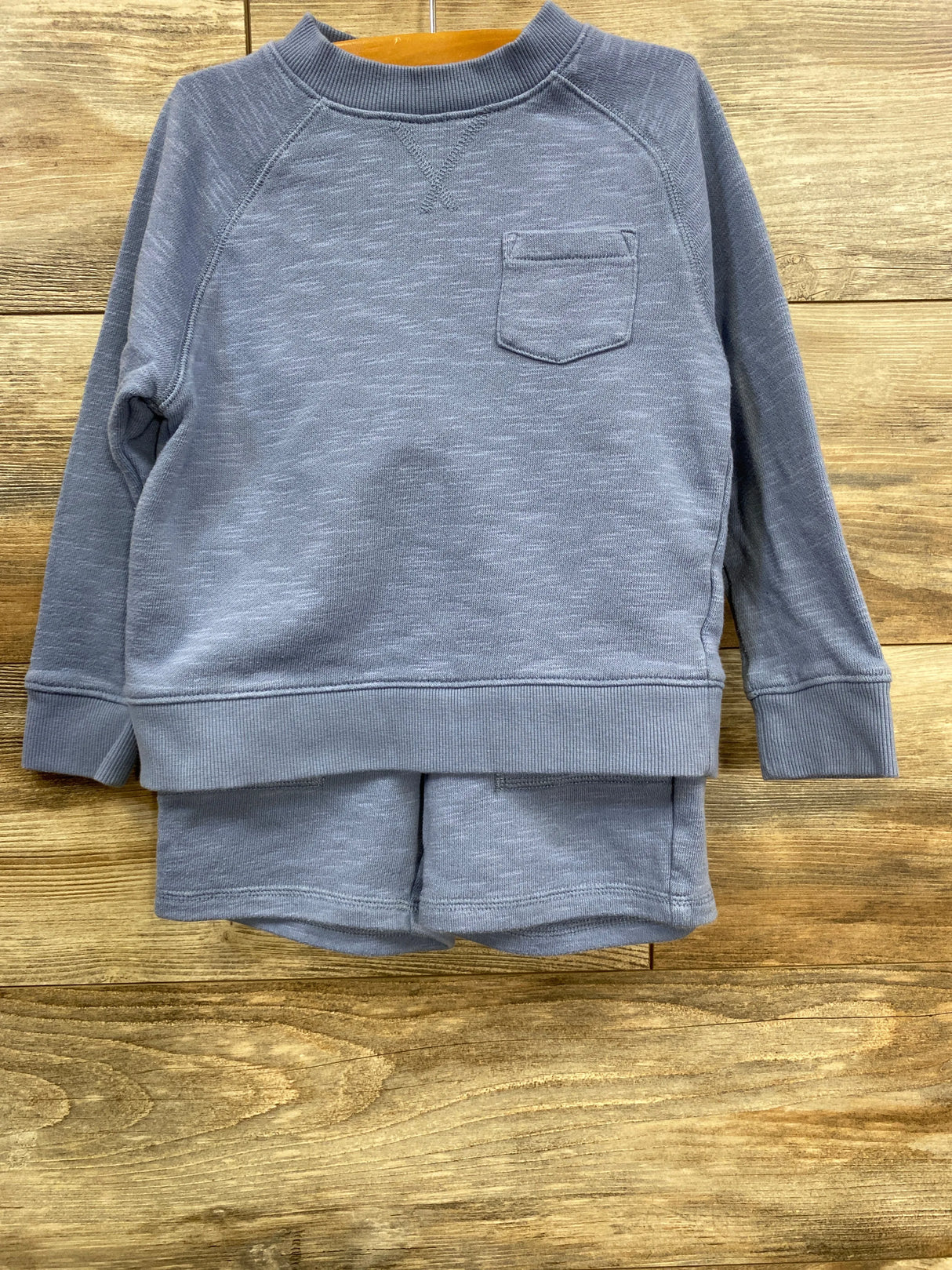 Blue cozy long-sleeve sweatshirt and matching shorts set on wooden floor background