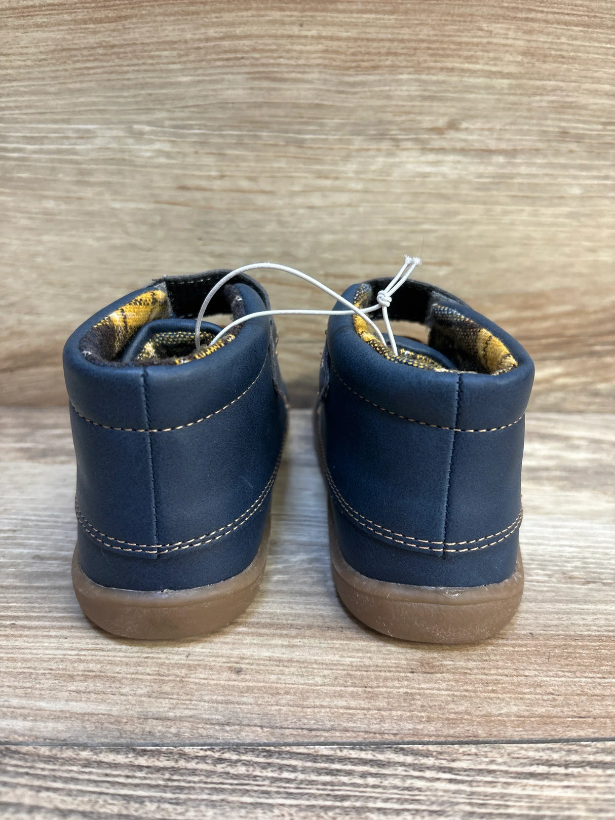 Rear view of kids navy blue boots with brown soles on wooden background