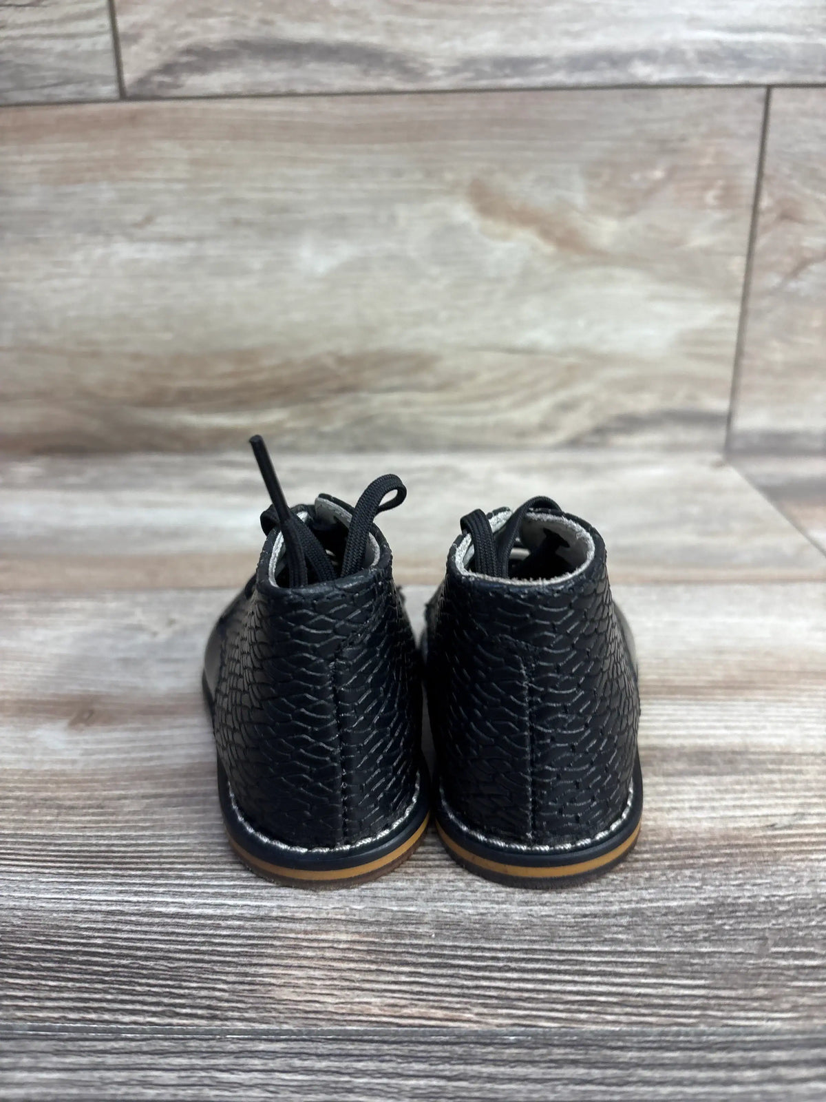 Back view of black textured toddler lace-up shoes on wooden floor