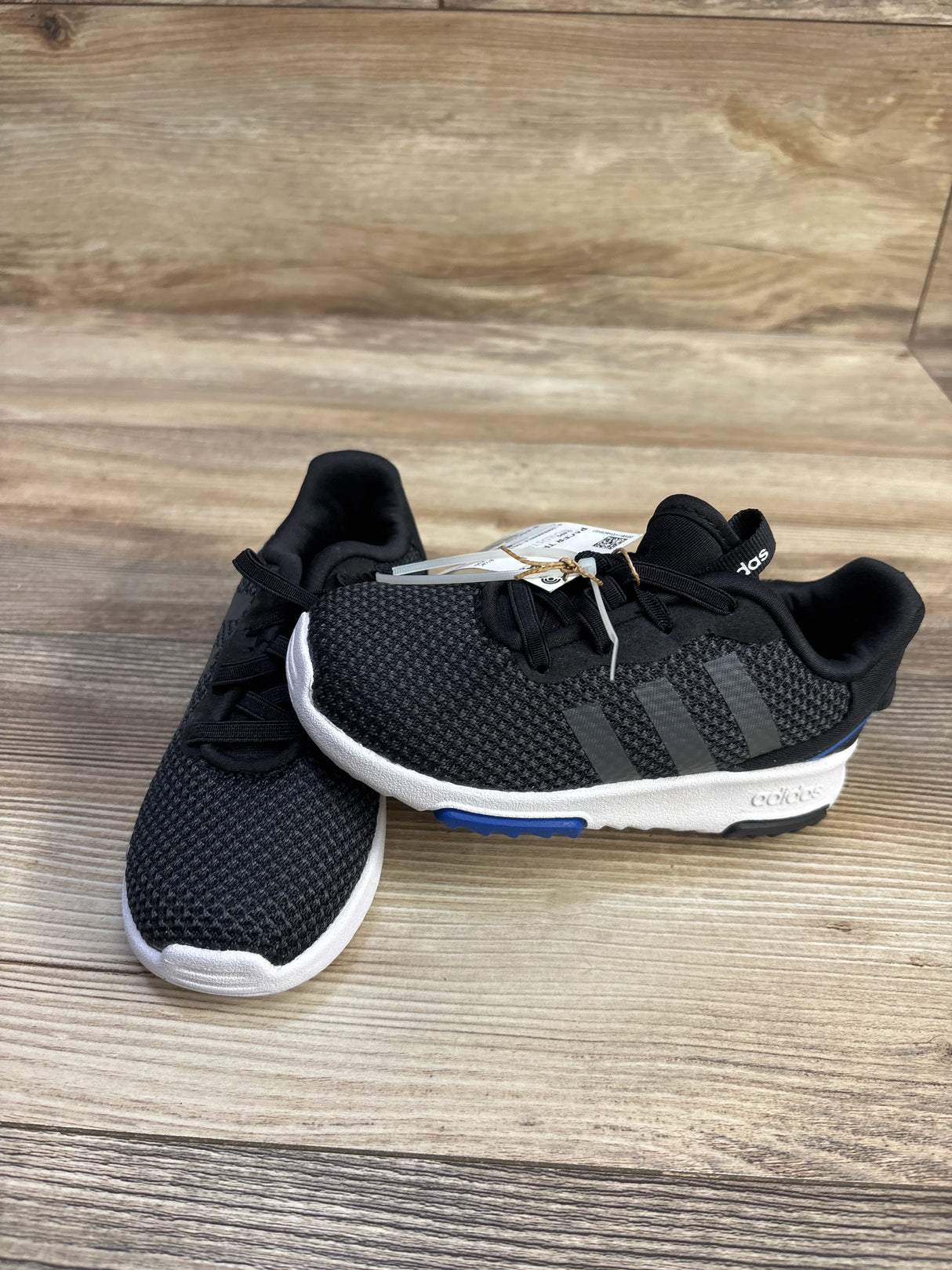Angled side view of Adidas Racer TR toddler sneakers showcasing black knit upper, white midsole and blue outsole accent on wood floor