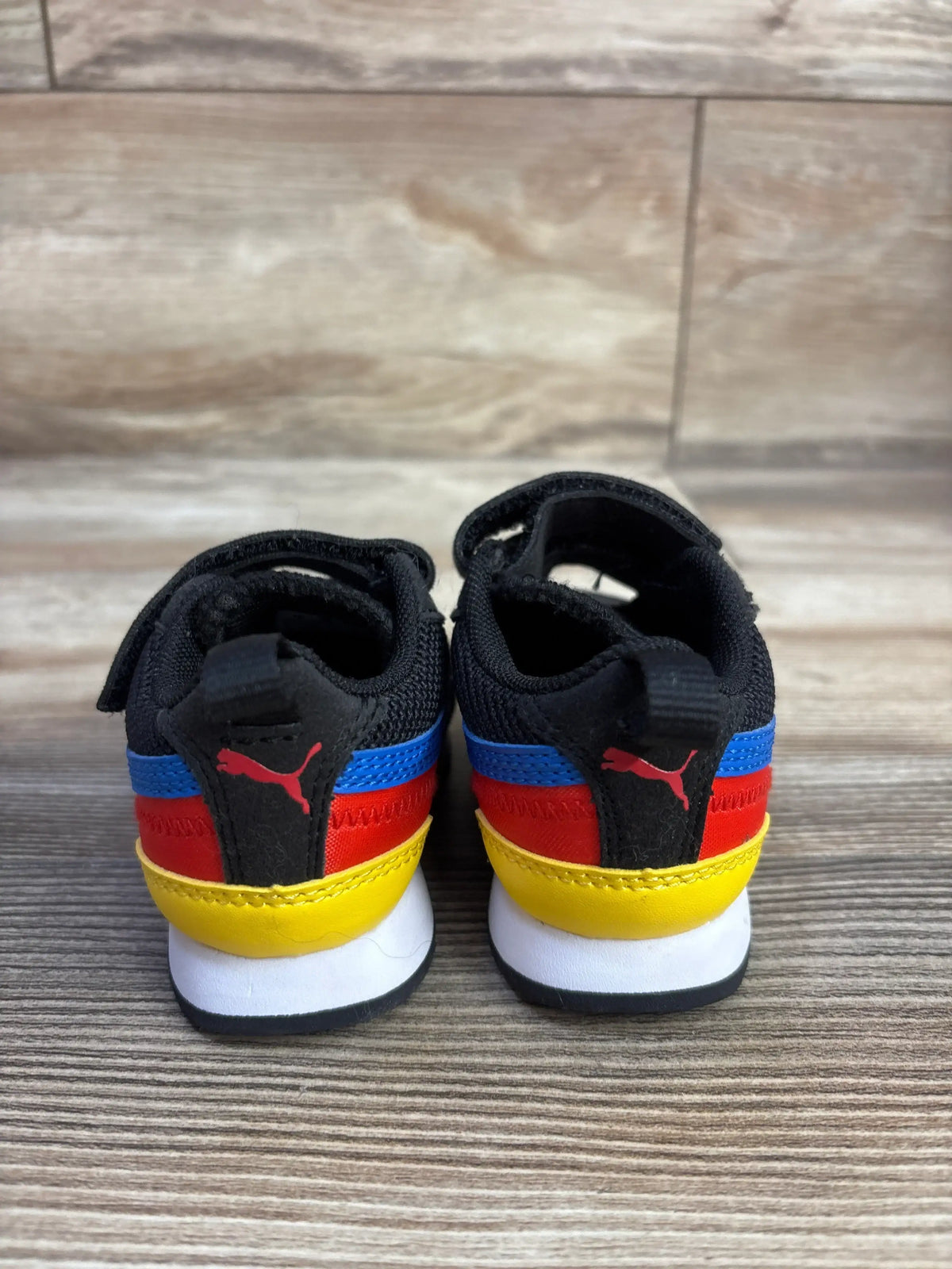 Rear view of Puma R78 double strap sneakers in black and size 3C showcasing multicolor heel accents on a wood floor