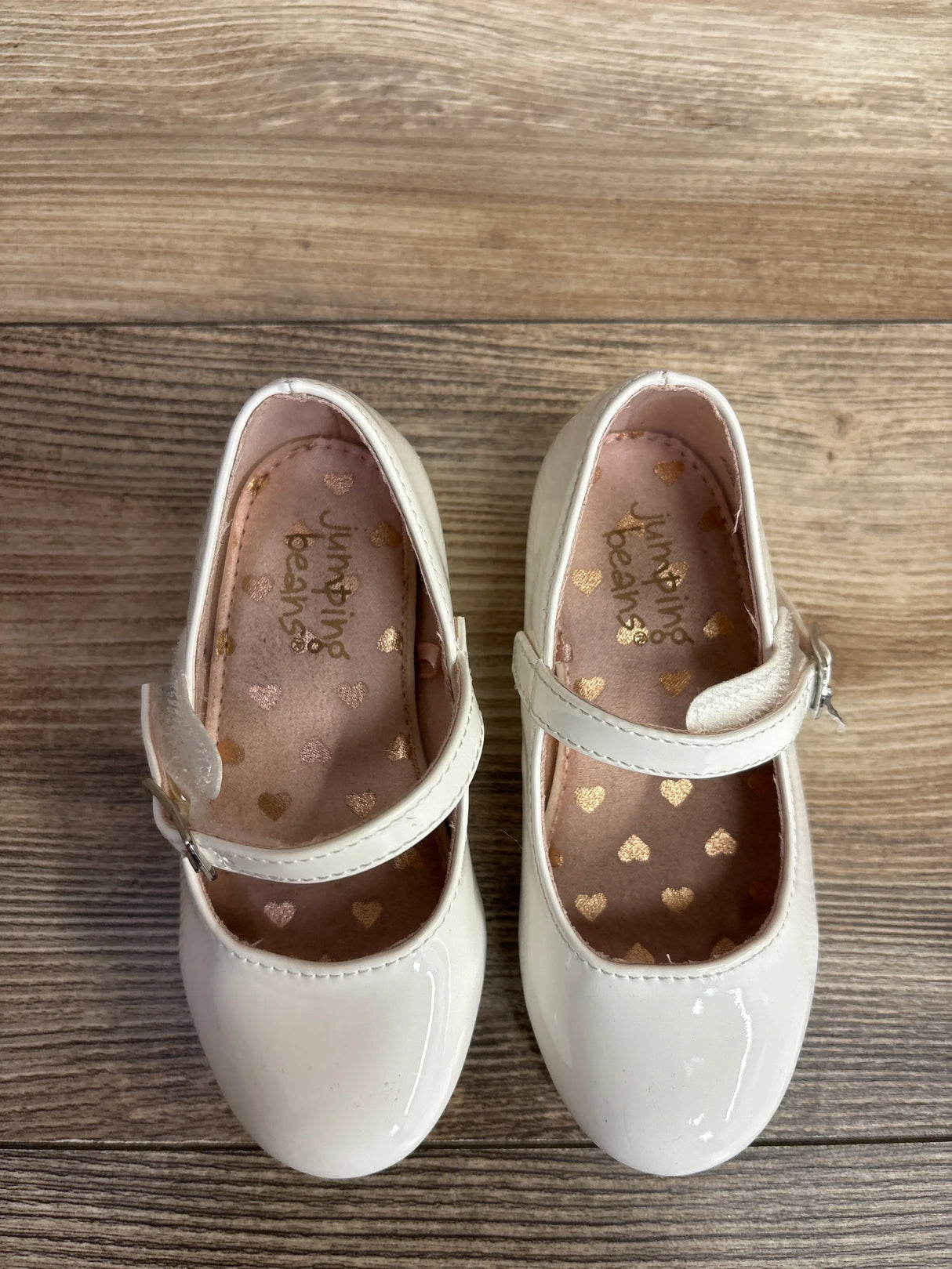 White patent leather toddler Mary Jane shoes with gold heart insoles on wood floor