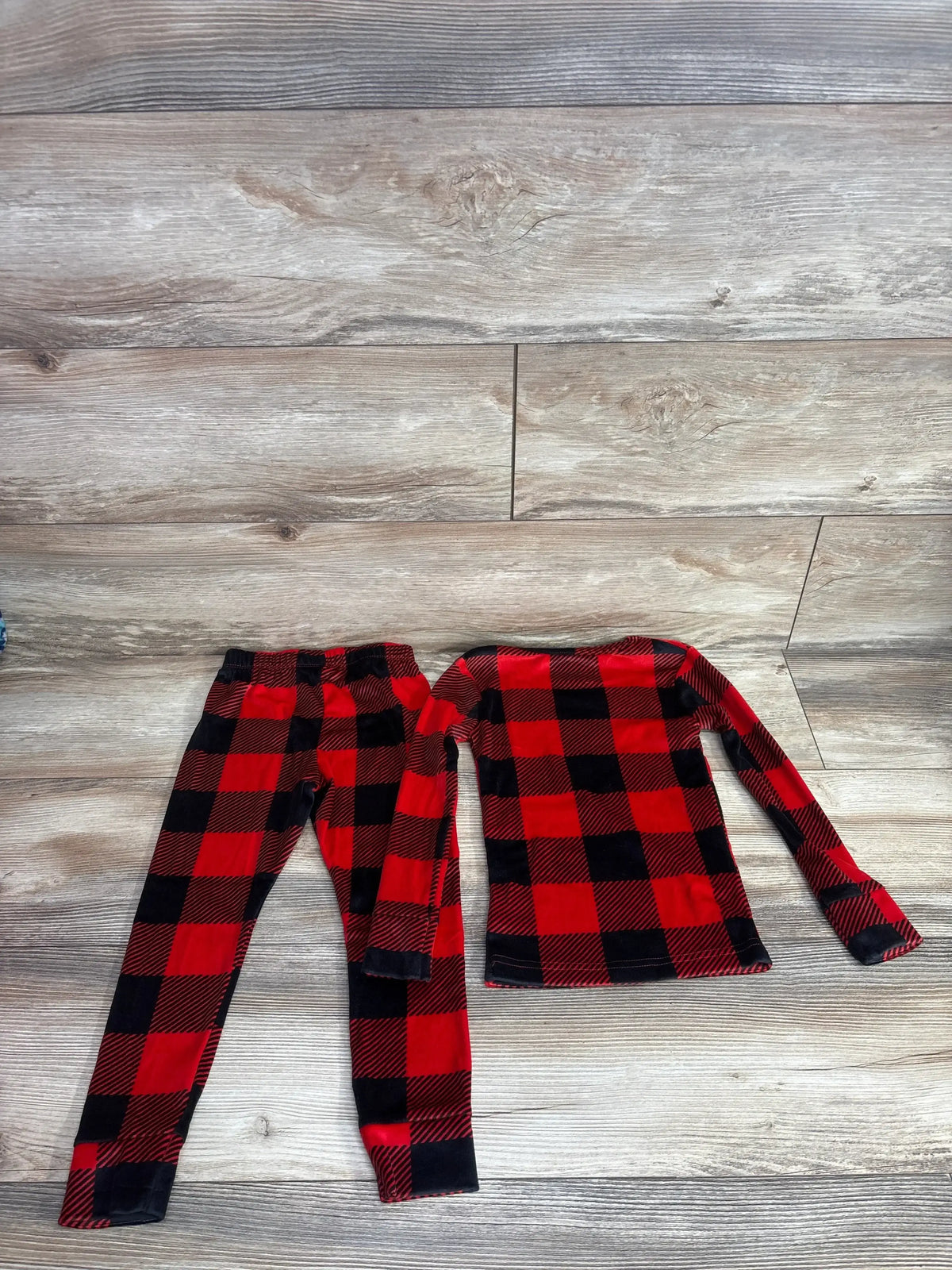 Flat lay of Cat and Jack 2pc Velour Pajama Set sz 4T showcasing red and black buffalo plaid long sleeve top and matching pants on wood plank floor
