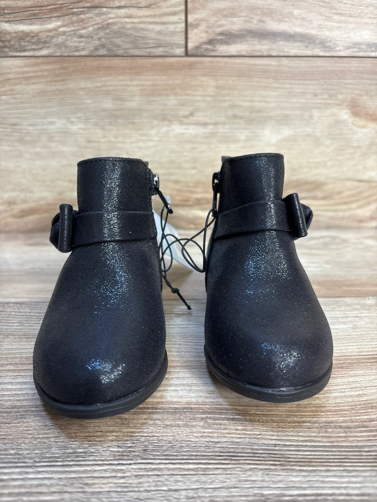 Pair of black toddler ankle boots with side bow detail on wood background