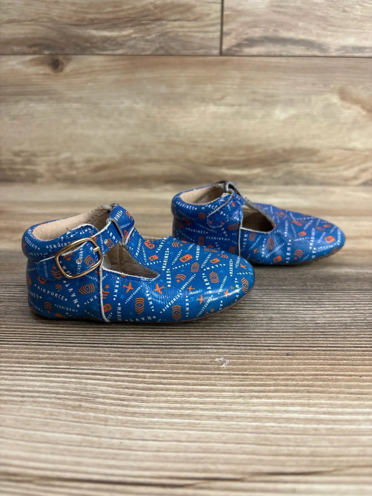 Blue baby shoes with military print, soft sole, and buckle, on wood background.