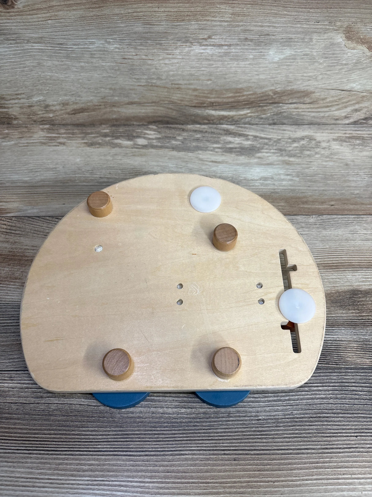 Wooden toy base with four pegs, round blue wheels, and sliding white knobs on wood background