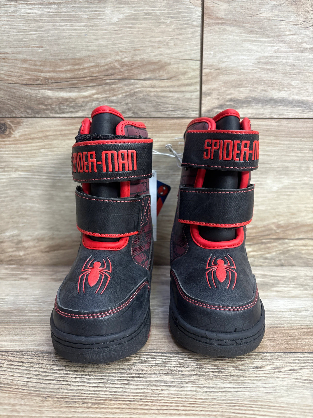 Pair of black and red Spider-Man kids boots with spider logo and Velcro straps on wooden surface