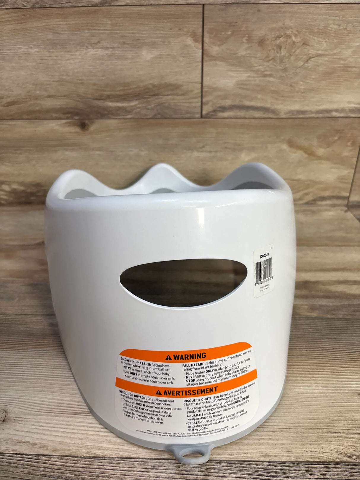 White baby bath seat with orange warning label on wood floor