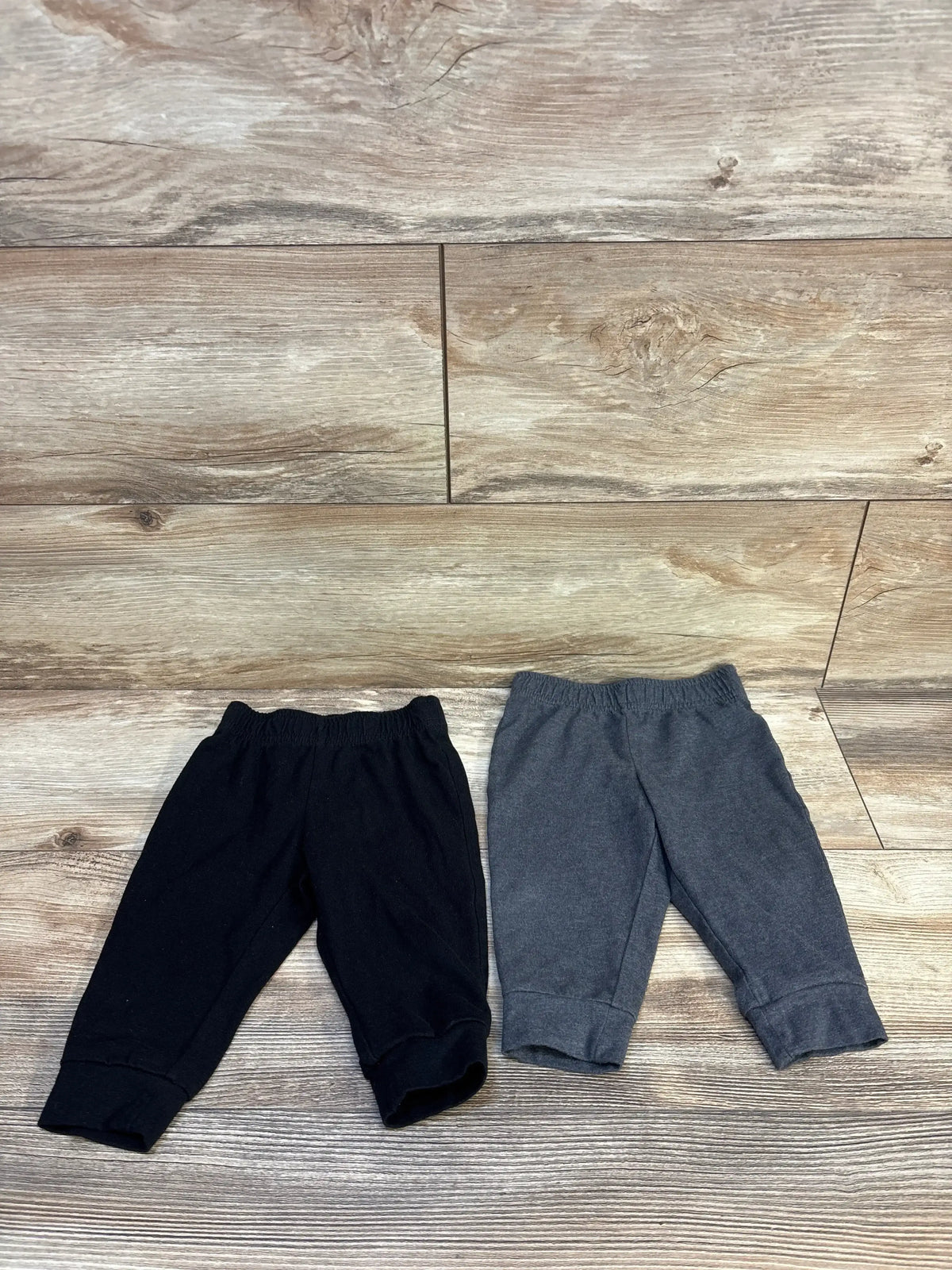 Black and gray baby jogger pants for infants, soft cotton blend with elastic waist and cuffs, laid flat on wood floor.