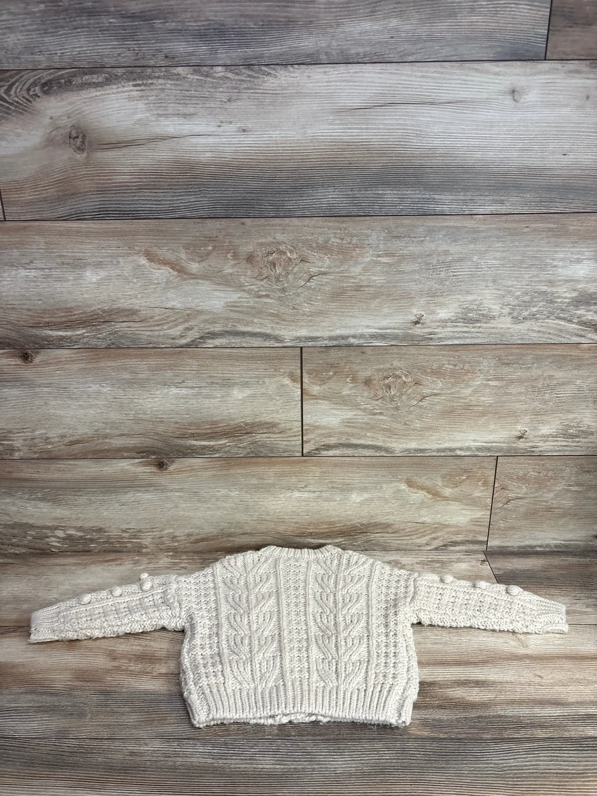 Flat lay back view of Rylee + Cru Bobble Cardigan in sand, cable knit with bobble sleeve details on wood background