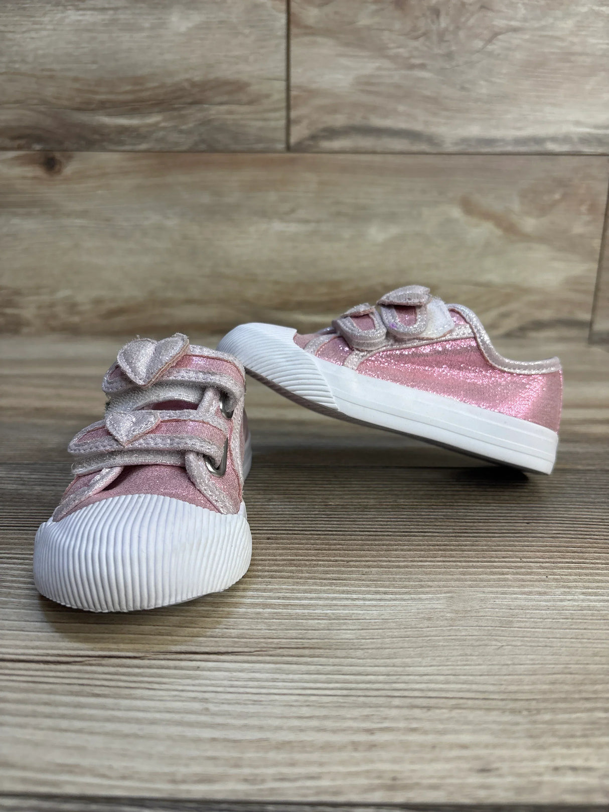 Pink glitter toddler sneakers with heart-shaped velcro straps on wooden floor