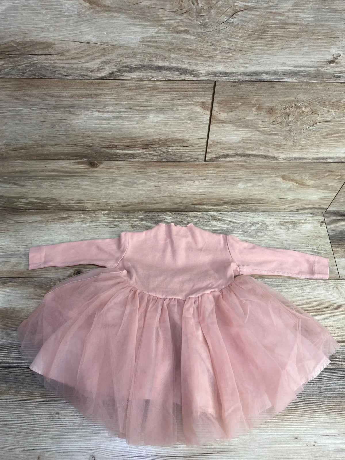 Pink long-sleeve baby dress with a soft tulle tutu skirt on wooden floor background