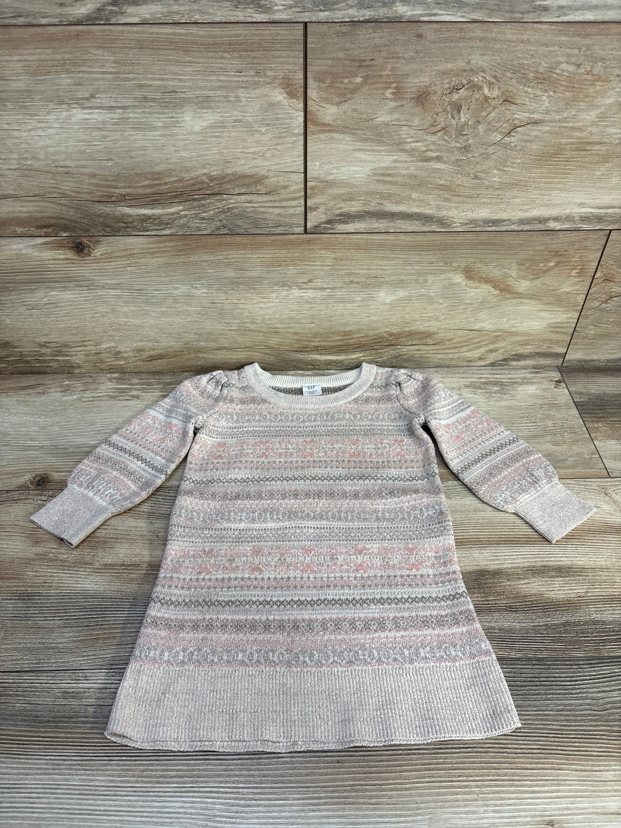 Girls' long sleeve knit sweater dress with pink and grey fair isle pattern, laid flat on wood