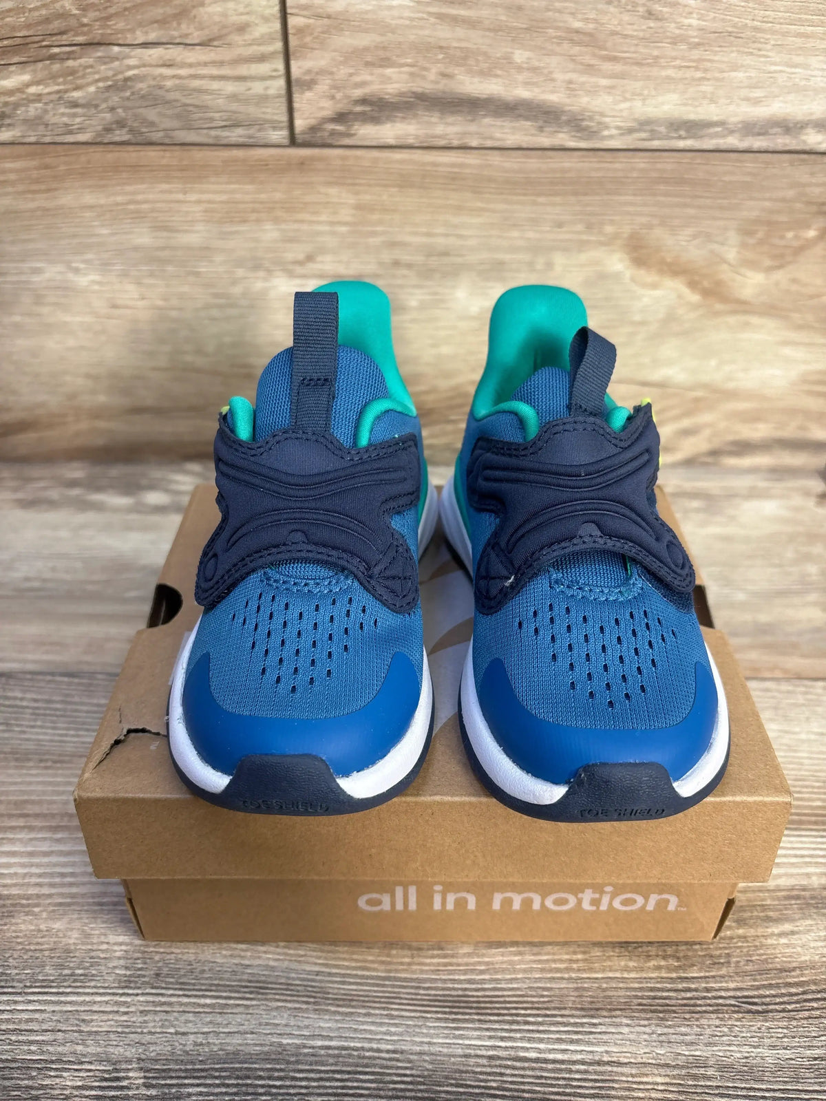 Front view of All In Motion Quinn kids sneakers, blue and teal, showing hook and loop strap and padded collar on an 'all in motion' shoe box
